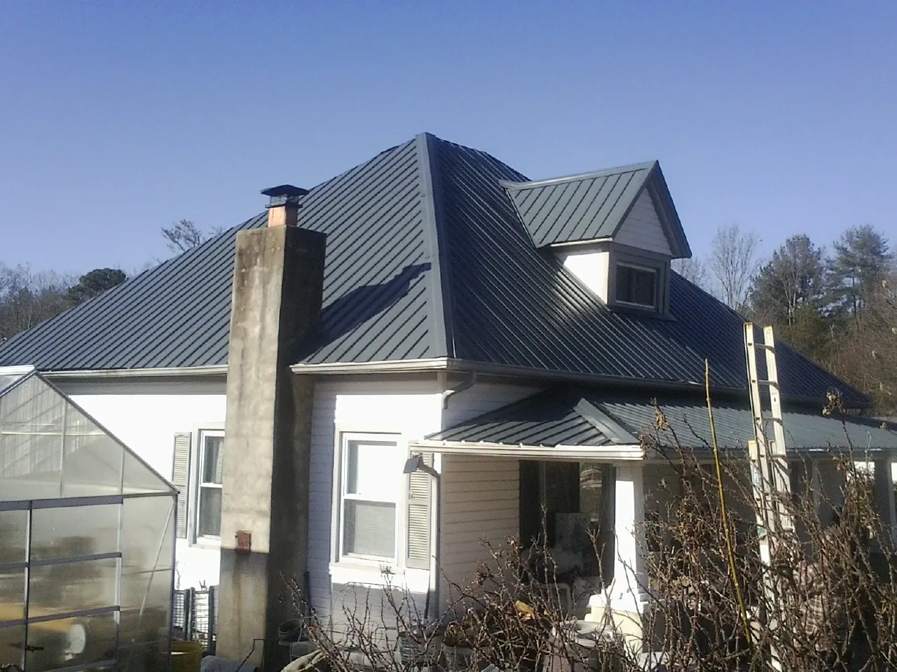 Dark blue standing seam metal roof on a white farmhouse with dormer — Slate & Tile Roof Repair by Roofing Brothers in Corolla