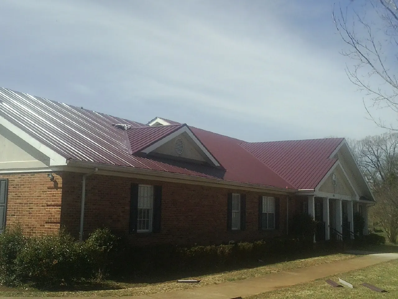 Red metal roof with gabled entries on a long brick building, from a Hail Damage Roof Repair job in Corolla