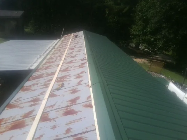 Old rusted panels beside newly installed green metal roofing — Wind Damage Roof Repair by Roofing Brothers in Corolla