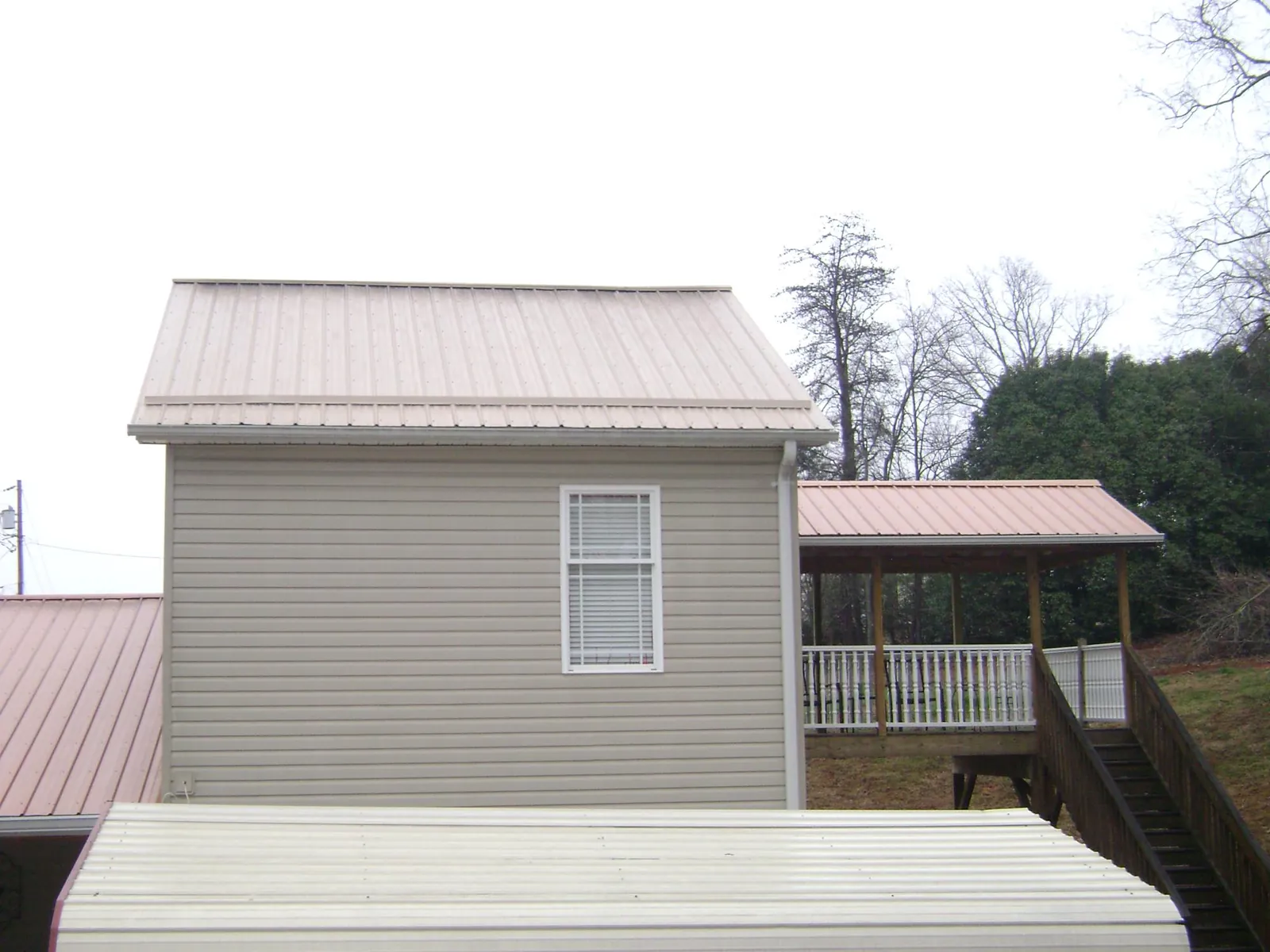 Tan metal roofs on a two story addition and attached porch, from a Roof Replacement job in Corolla